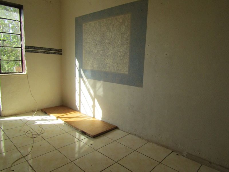 An empty bedroom featuring tiled flooring and a steel-framed window, requiring cosmetic updates and wall repairs to restore its appeal.