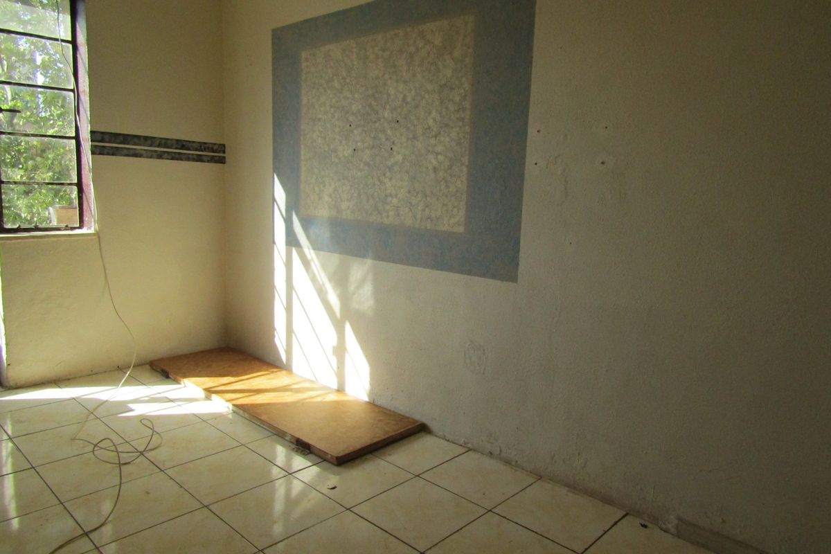 An empty bedroom featuring tiled flooring and a steel-framed window, requiring cosmetic updates and wall repairs to restore its appeal.