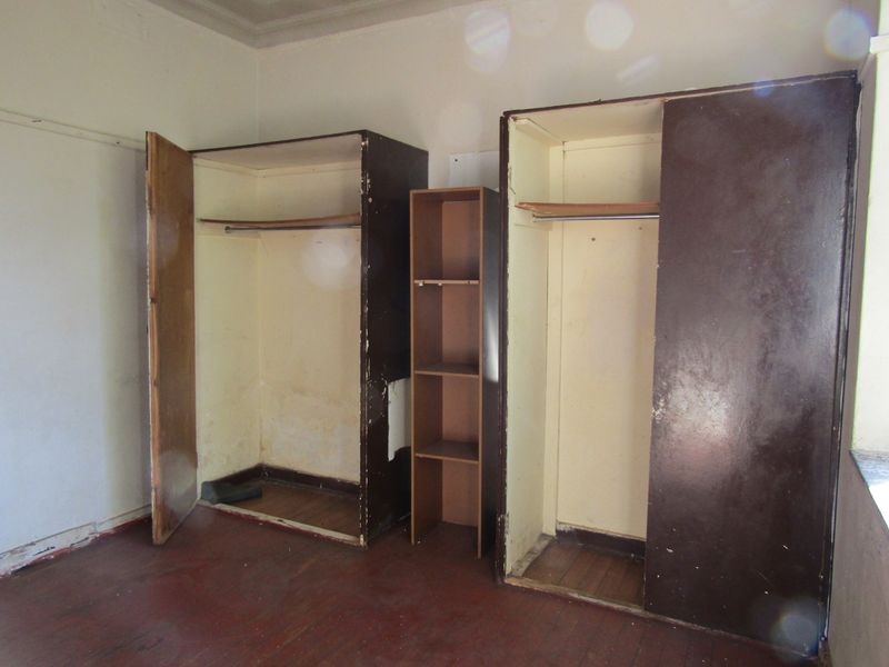A bedroom featuring original wooden flooring and dated built-in cupboards in need of refurbishment or replacement.