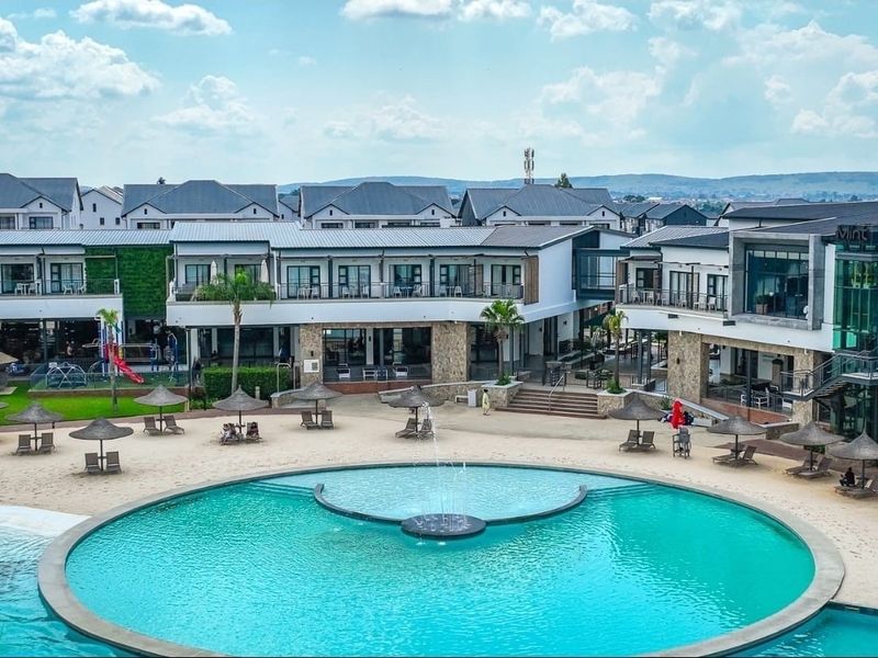 A well-maintained apartment complex featuring a large central swimming pool with a fountain, surrounded by landscaped grounds and modern building facades.