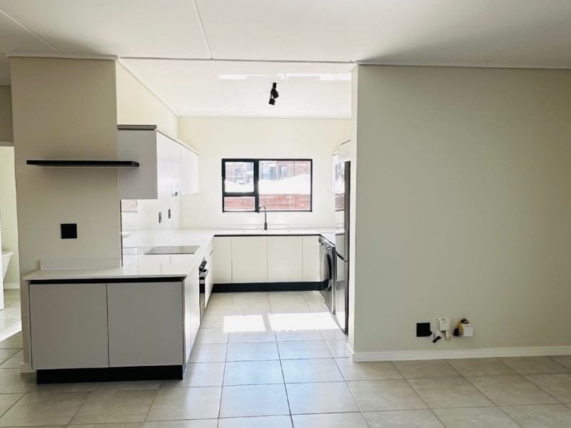 A modern, clean-lined kitchen featuring white cabinetry, stone countertops, and neutral ceramic floor tiles, offering a bright and functional workspace.