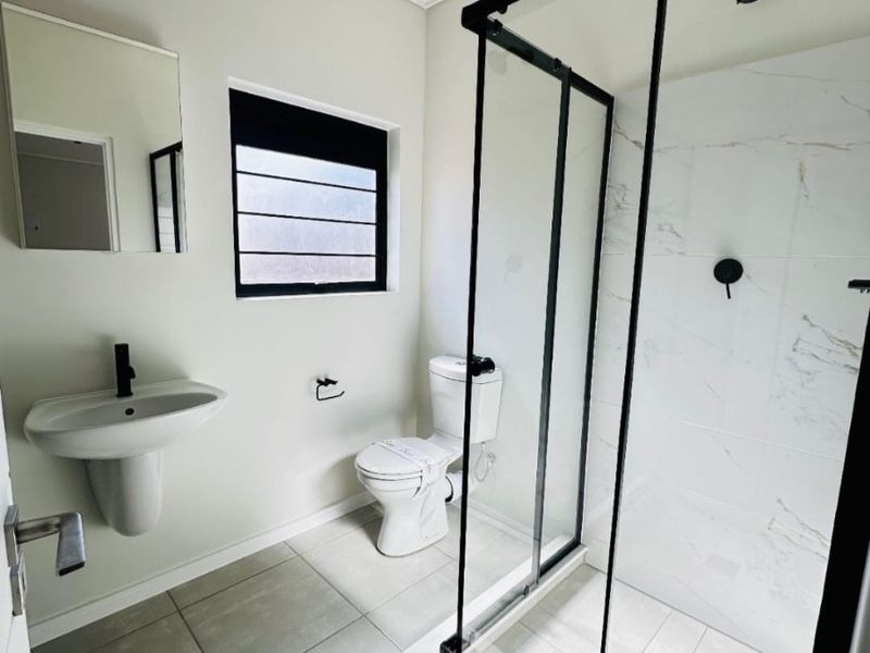 Modern bathroom featuring a walk-in shower with black frame, pedestal basin, toilet, and neutral floor tiles.