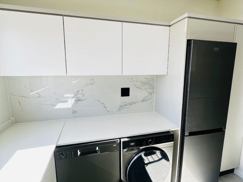 A modern, well-maintained laundry area featuring sleek white cabinetry, marble-look splashback, stone-look countertops, and tiled flooring.