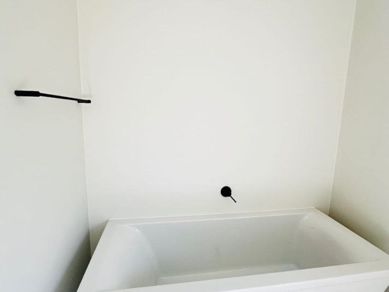 A clean, modern bathroom featuring a white freestanding bathtub with matte black wall-mounted fixtures and neutral floor tiling.