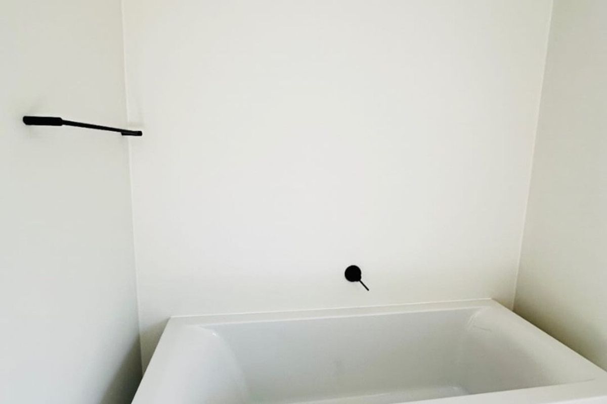 A clean, modern bathroom featuring a white freestanding bathtub with matte black wall-mounted fixtures and neutral floor tiling.