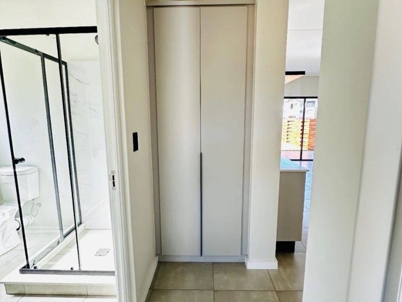 A clean, neutral hallway featuring built-in storage cupboards and direct access to an adjacent modern bathroom with a glass shower enclosure.