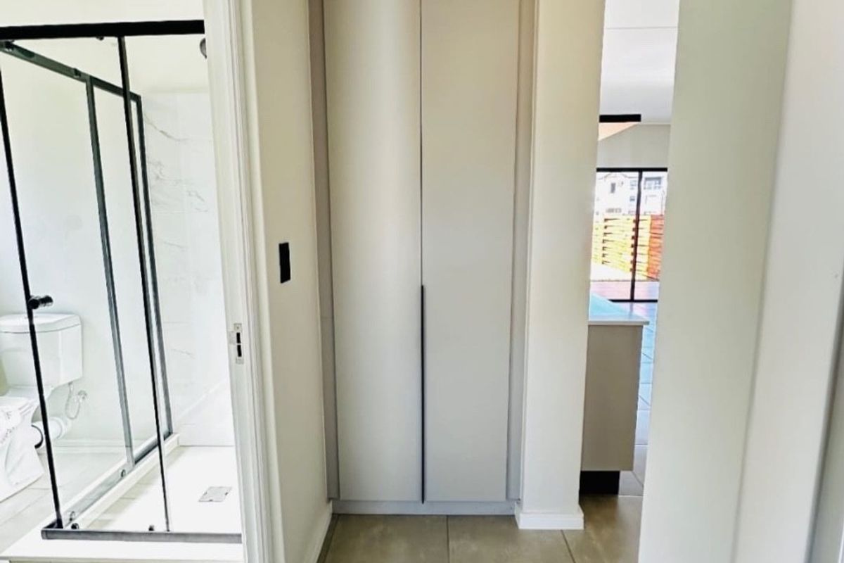 A clean, neutral hallway featuring built-in storage cupboards and direct access to an adjacent modern bathroom with a glass shower enclosure.