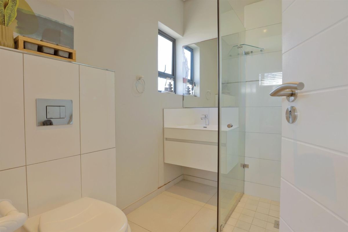 Modern bathroom featuring a wall-hung toilet with concealed cistern, a floating vanity with basin, and a glass-enclosed shower with tiled finishes.