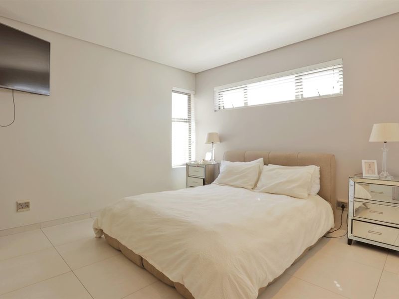 A bright and modern bedroom featuring neutral wall tones, tiled flooring, and horizontal window blinds, providing a clean and comfortable living space.