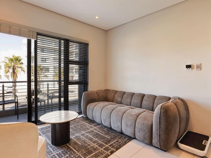 A bright and modern living room featuring large sliding glass doors that open onto a private balcony, complemented by neutral tiled flooring and recessed lighting.