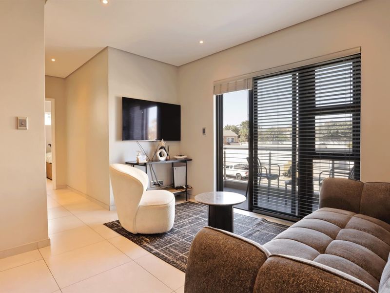 Modern living room featuring tiled flooring, recessed downlights, and a sliding glass door providing access to a balcony.