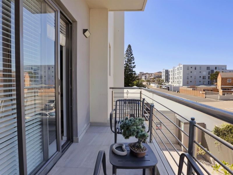 A modern apartment balcony featuring tiled flooring, a metal safety railing, and a sliding glass door providing access to the interior.