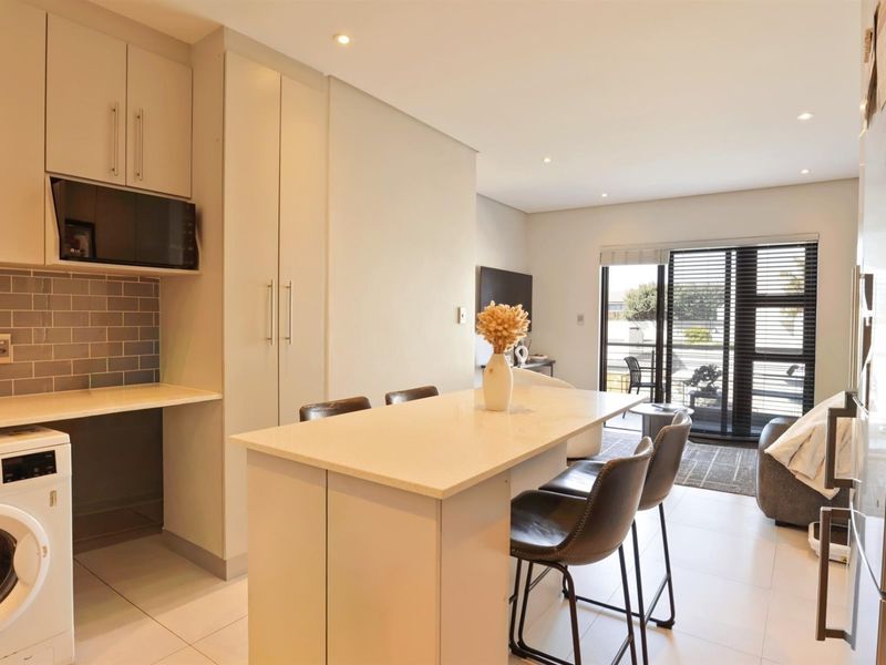 Modern open-plan apartment featuring a sleek kitchen with stone countertops, subway tile backsplash, and integrated laundry, flowing into a bright living area with balcony access.