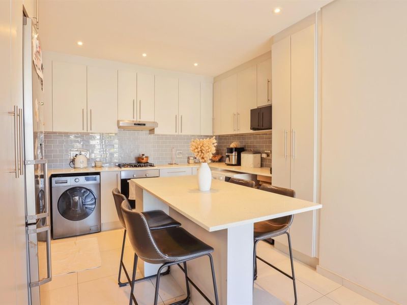 Modern kitchen featuring white cabinetry, stone countertops, subway tile backsplash, integrated appliances, and a central breakfast island with seating.