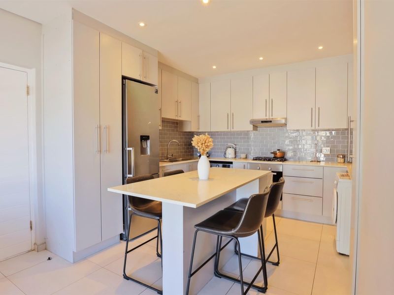 Modern kitchen featuring light-toned cabinetry, stone countertops, subway tile backsplash, integrated appliances, and a central island with breakfast bar seating.