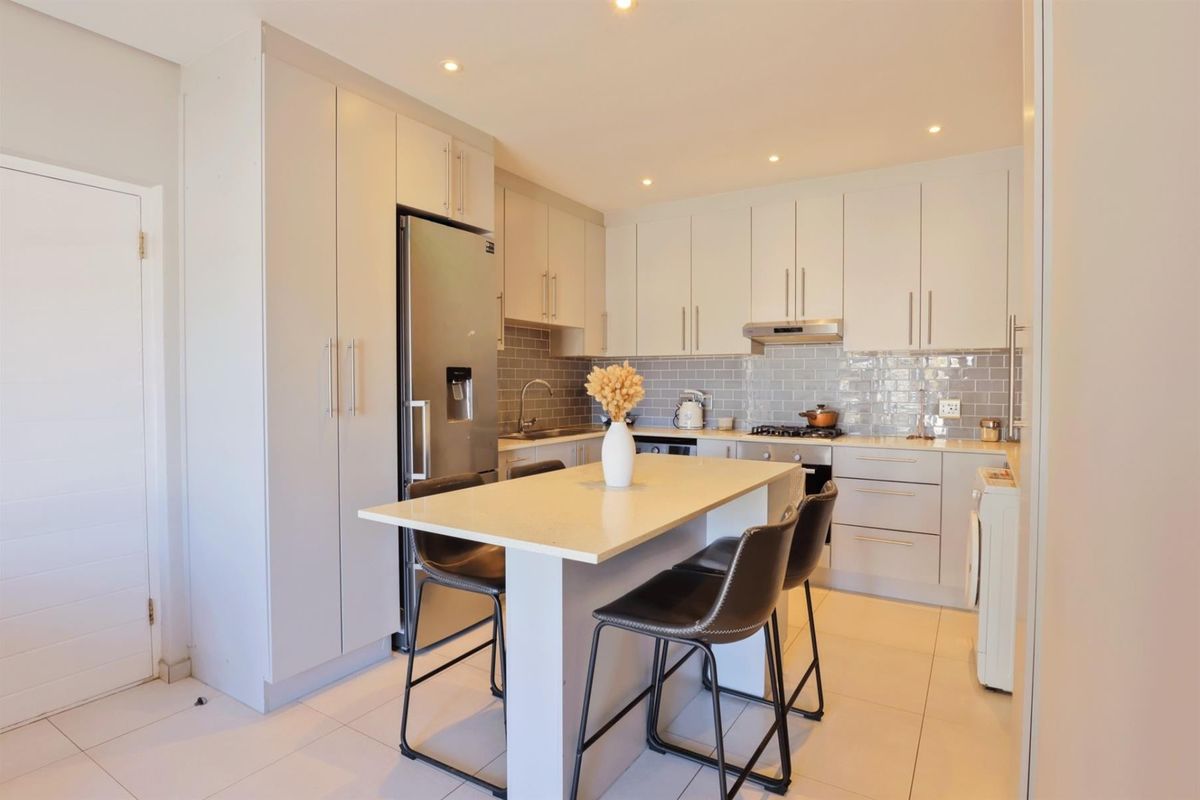 Modern kitchen featuring light-toned cabinetry, stone countertops, subway tile backsplash, integrated appliances, and a central island with breakfast bar seating.