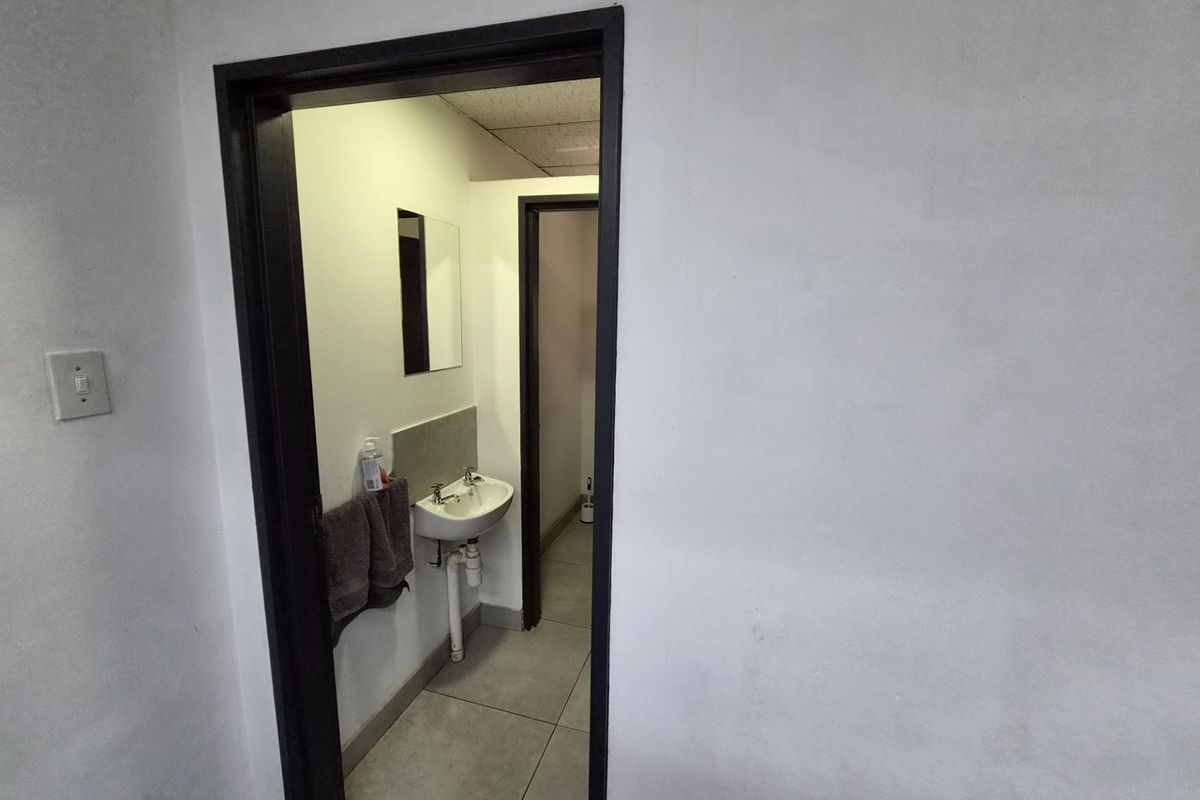 A functional bathroom space featuring a wall-mounted basin, tiled flooring, and a mirror, accessible through a doorway.