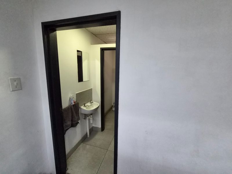 A functional bathroom space featuring a wall-mounted basin, tiled flooring, and a mirror, accessible through a doorway.