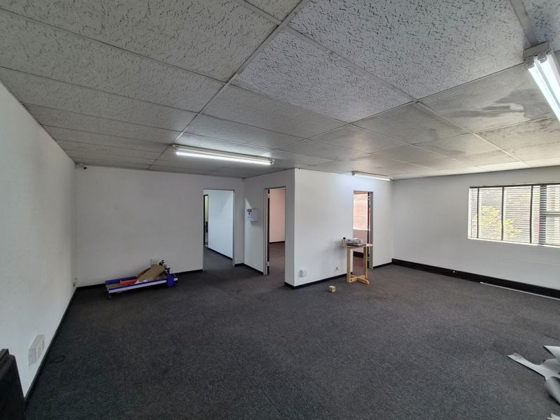 An open-plan office space featuring a suspended ceiling, fluorescent lighting, and carpeted flooring, offering a functional layout for various business operations.