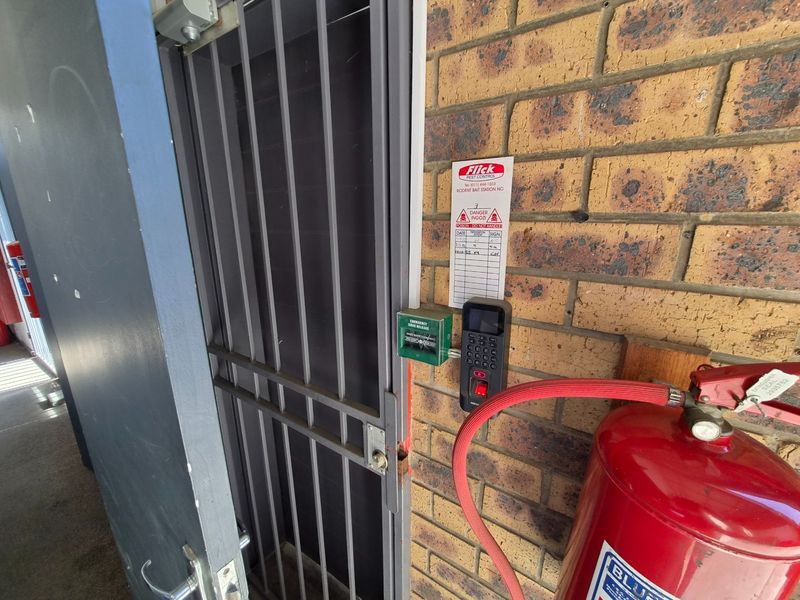 Industrial entry point featuring a security gate, keypad access control system, emergency release button, and wall-mounted fire safety equipment.