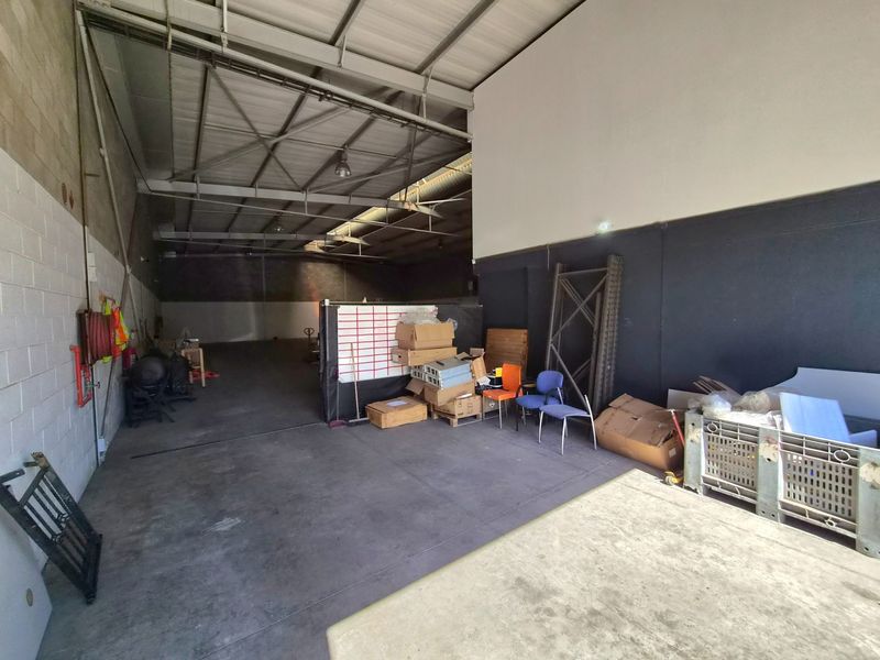 Spacious industrial utility area featuring high-clearance ceilings, exposed steel roof trusses, and durable concrete flooring, suitable for storage or workshop operations.