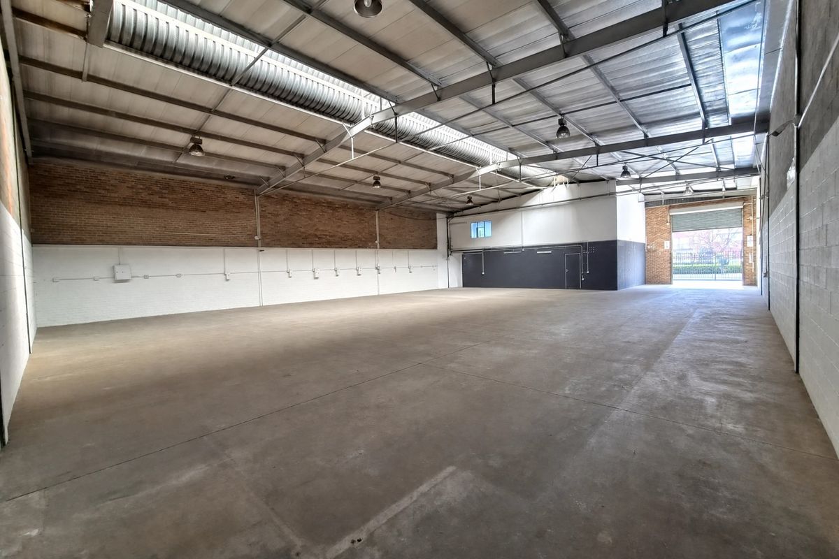 Spacious industrial warehouse unit featuring high ceilings with exposed steel trusses, concrete flooring, and a large roller shutter door for easy access.