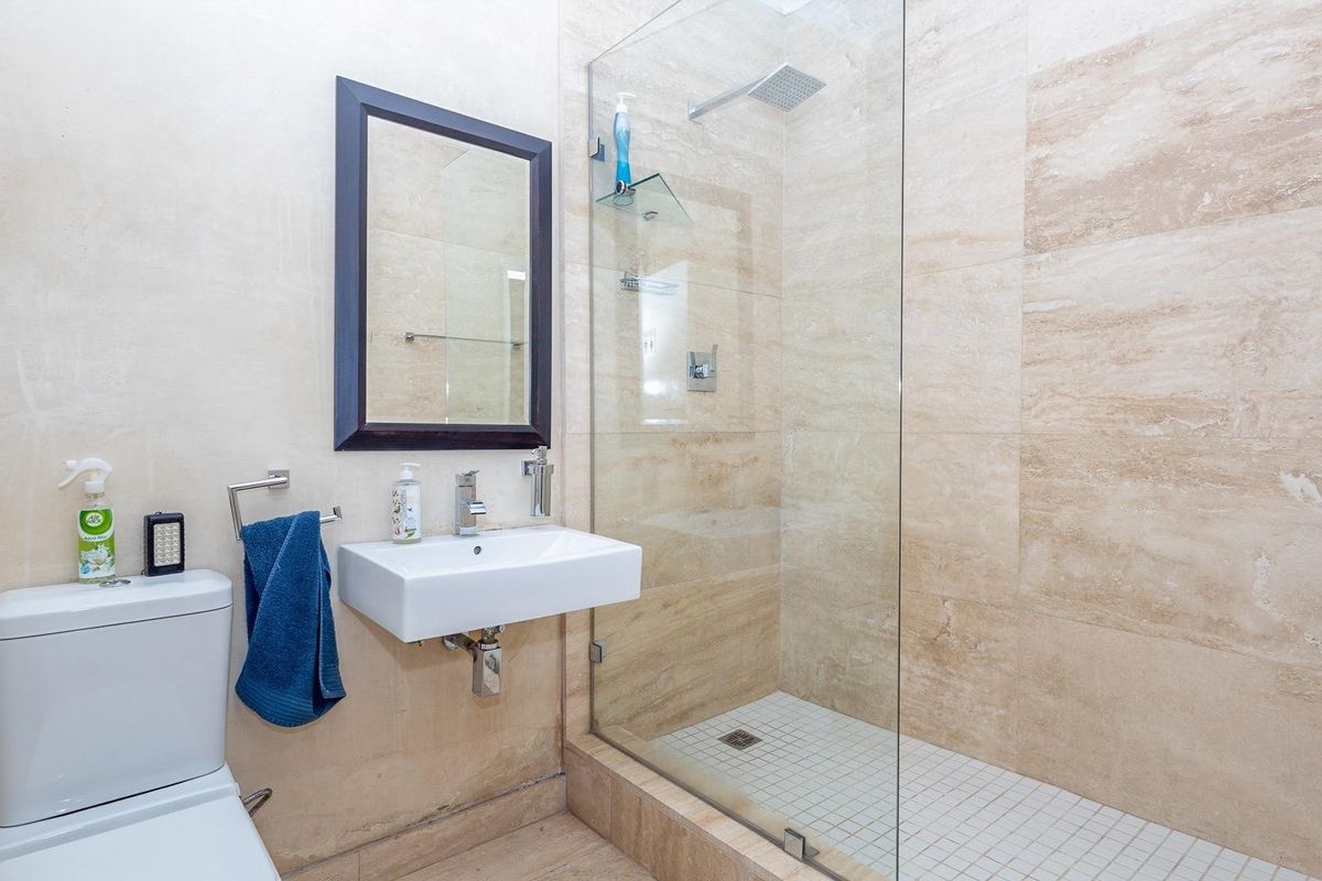 Modern bathroom featuring a wall-mounted basin, a spacious glass-enclosed shower with a rain shower head, and neutral floor-to-ceiling tiling.