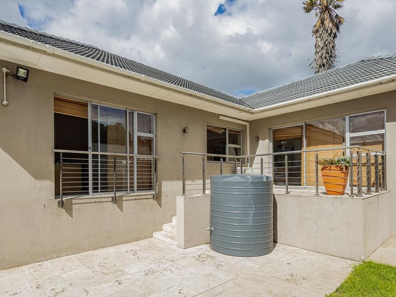 Rear exterior view featuring a paved patio area, stainless steel balustrades, and a water storage tank adjacent to the building facade.
