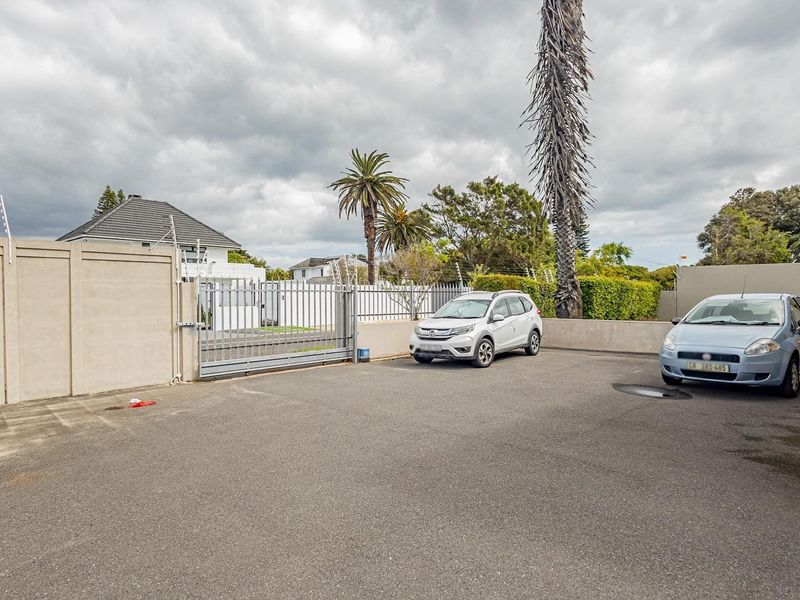 A paved rear parking area featuring a secure perimeter wall with electric fencing and a sliding gate entrance.