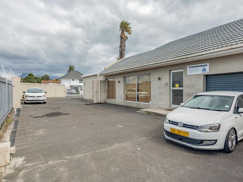 Front exterior view of the office property featuring an asphalt driveway, secure perimeter fencing, and a roller shutter garage door.