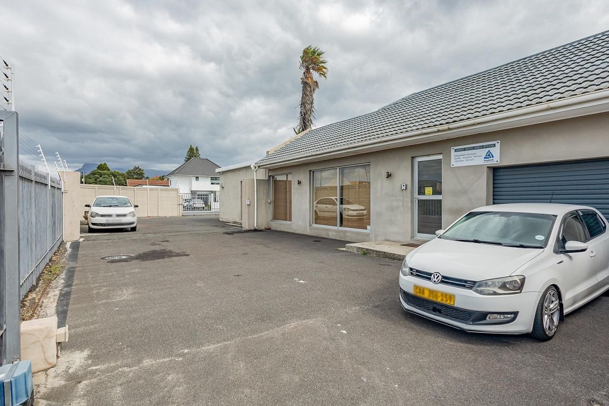 Front exterior view of the office property featuring an asphalt driveway, secure perimeter fencing, and a roller shutter garage door.