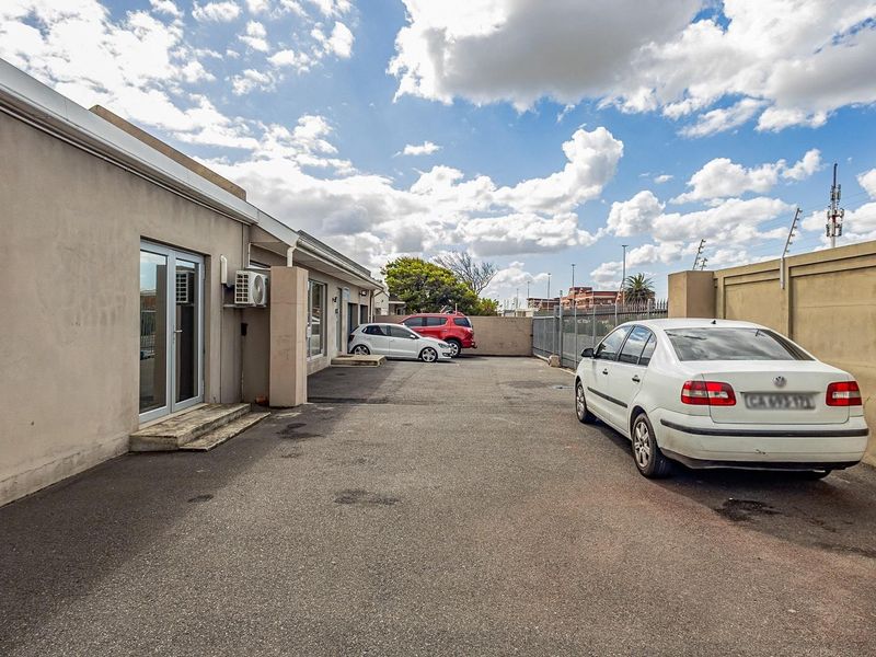 Rear exterior view of the office property featuring an asphalt parking area, perimeter wall with electric fencing, and external access via glass sliding doors.