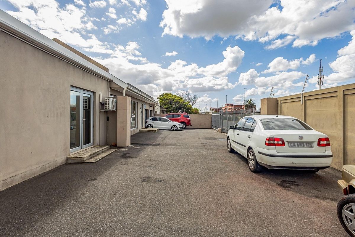 Rear exterior view of the office property featuring an asphalt parking area, perimeter wall with electric fencing, and external access via glass sliding doors.