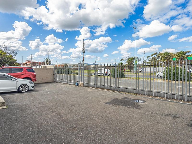 Exterior view of the office property featuring an asphalt parking area secured by steel fencing and a sliding gate.
