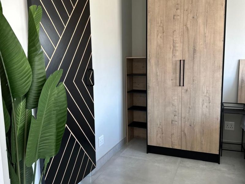 Modern bedroom featuring a stylish black sliding barn door, built-in wood-finish wardrobe, and neutral tiled flooring.