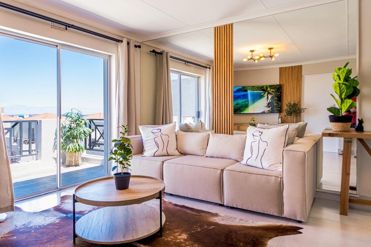 A bright living room featuring a large sliding glass door leading to a balcony, a mirrored wall, and decorative slatted wood paneling.
