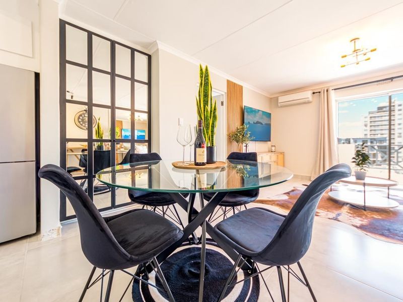 Bright open-plan living and dining area featuring tiled floors, modern mirror accents, and direct access to a balcony through sliding glass doors.