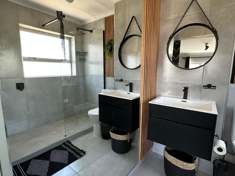 Modern bathroom featuring a double vanity with black cabinetry, a spacious walk-in shower with glass screen, and stylish timber slat wall accents.