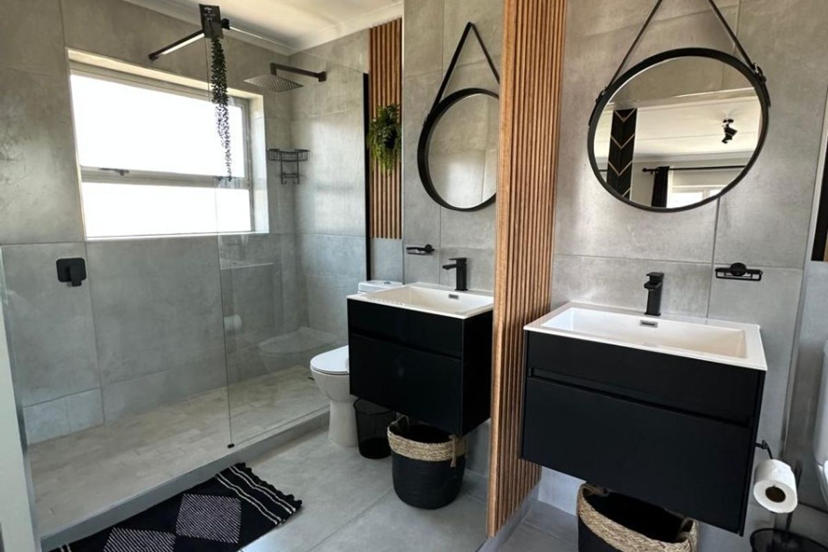 Modern bathroom featuring a double vanity with black cabinetry, a spacious walk-in shower with glass screen, and stylish timber slat wall accents.