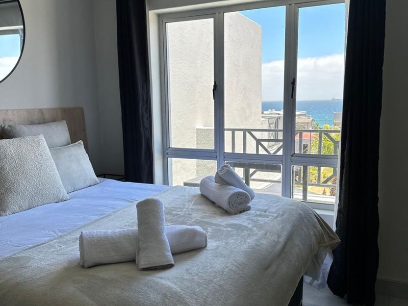 A bright bedroom featuring large windows with ocean views, neutral wall tones, and tiled flooring.