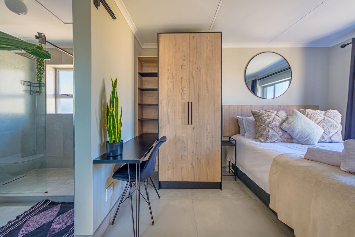 Modern bedroom featuring a built-in wardrobe, integrated desk, and an open-plan en-suite bathroom with a glass-enclosed shower.