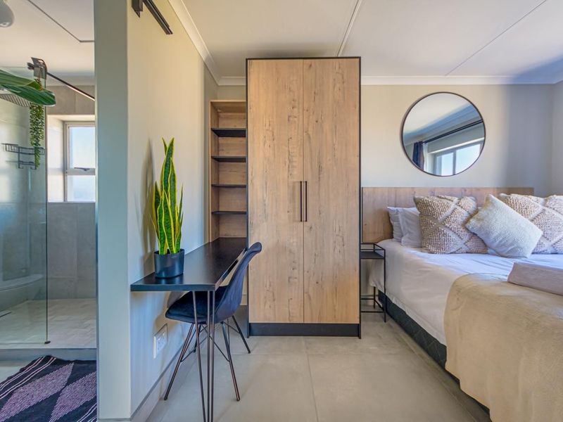 Modern bedroom featuring a built-in wardrobe, integrated desk, and an open-plan en-suite bathroom with a glass-enclosed shower.
