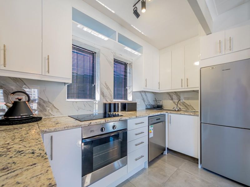 Modern kitchen featuring white cabinetry, granite countertops, marble-look splashback, and integrated appliances including an oven, hob, and dishwasher.