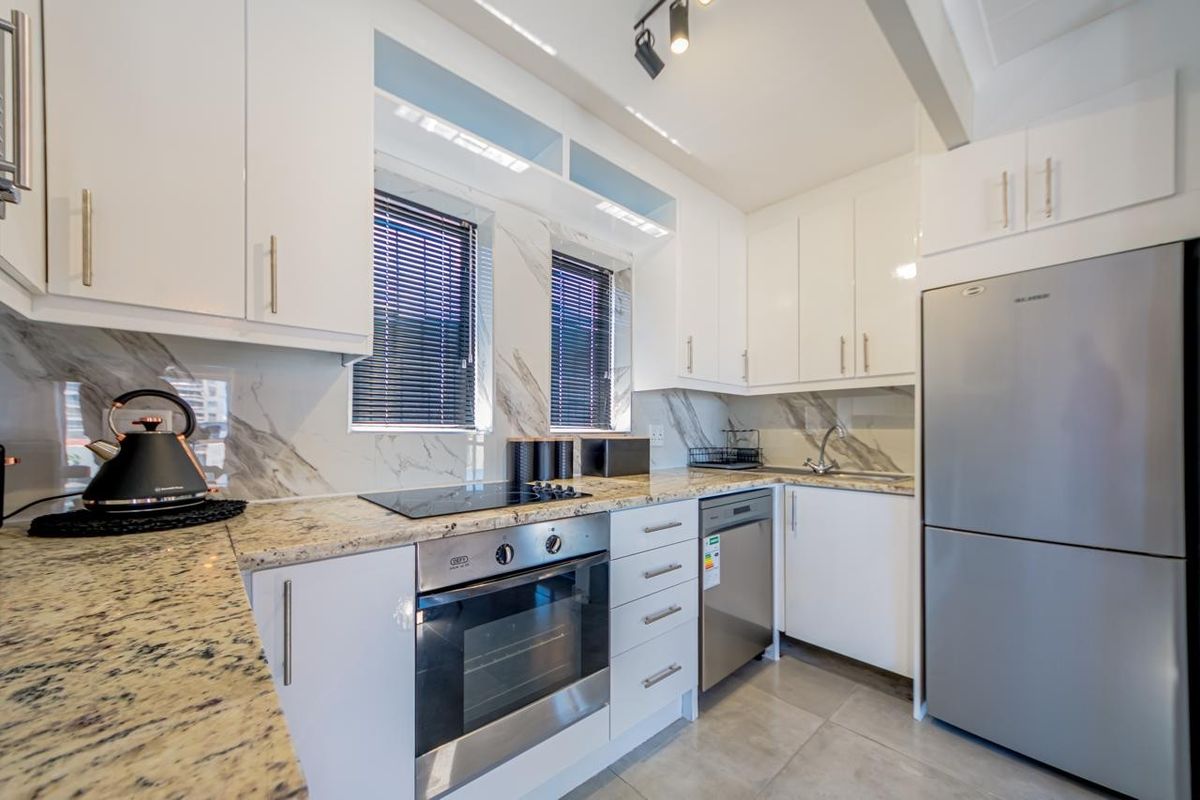 Modern kitchen featuring white cabinetry, granite countertops, marble-look splashback, and integrated appliances including an oven, hob, and dishwasher.