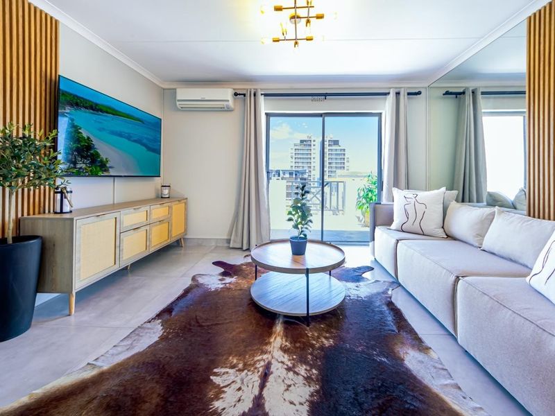 A modern, well-maintained living room featuring tiled floors, a slatted timber accent wall, mirrored paneling, and direct access to a balcony via sliding glass doors.