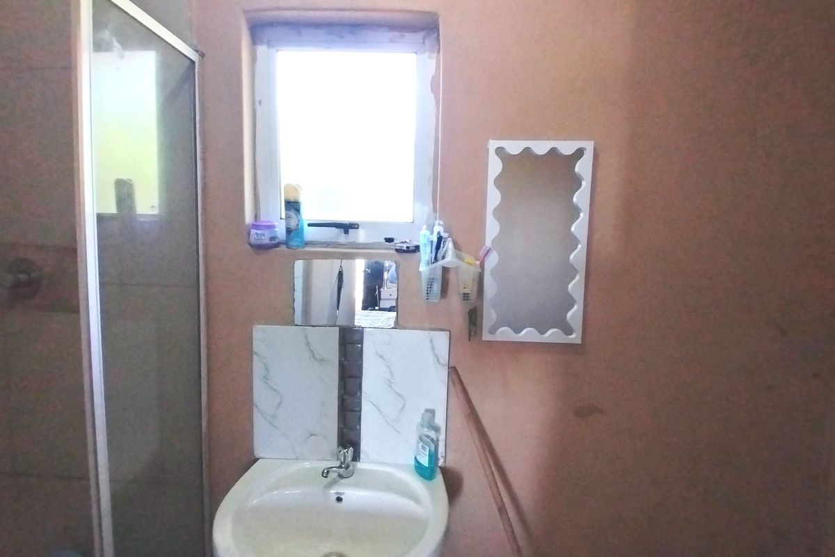 A compact bathroom featuring a shower enclosure and a pedestal basin with a tiled splashback, requiring cosmetic updates to the wall finishes.