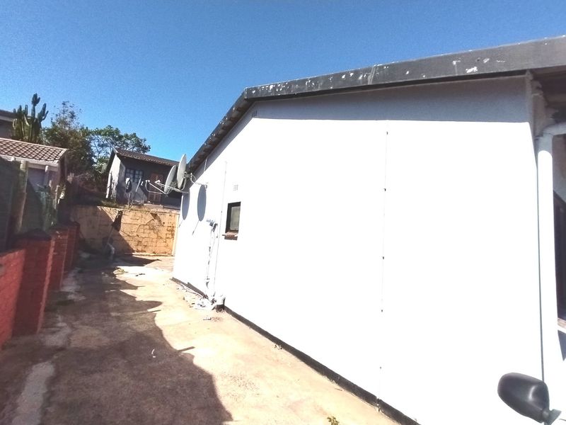A view of the rear exterior wall of the house, featuring a satellite dish, concrete paving, and a brick retaining wall.