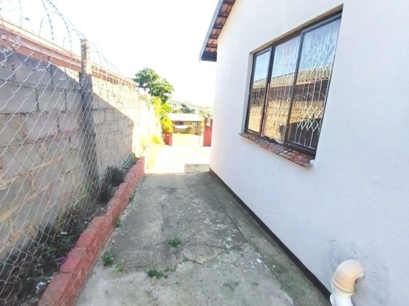 A narrow side passage featuring a concrete walkway, secured by a chain link fence with razor wire and a brick retaining wall.