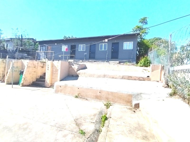 Rear exterior view of a multi-unit dwelling featuring concrete retaining walls, paved yard space, and perimeter chain link fencing with security wire.