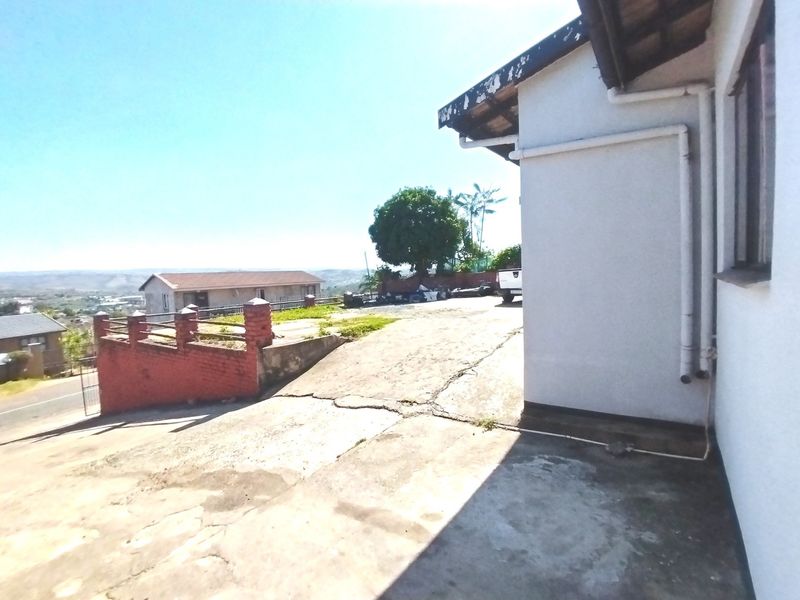 Exterior view of the property showing a concrete driveway, brick retaining wall, and building facade with visible wear on the roof fascia.